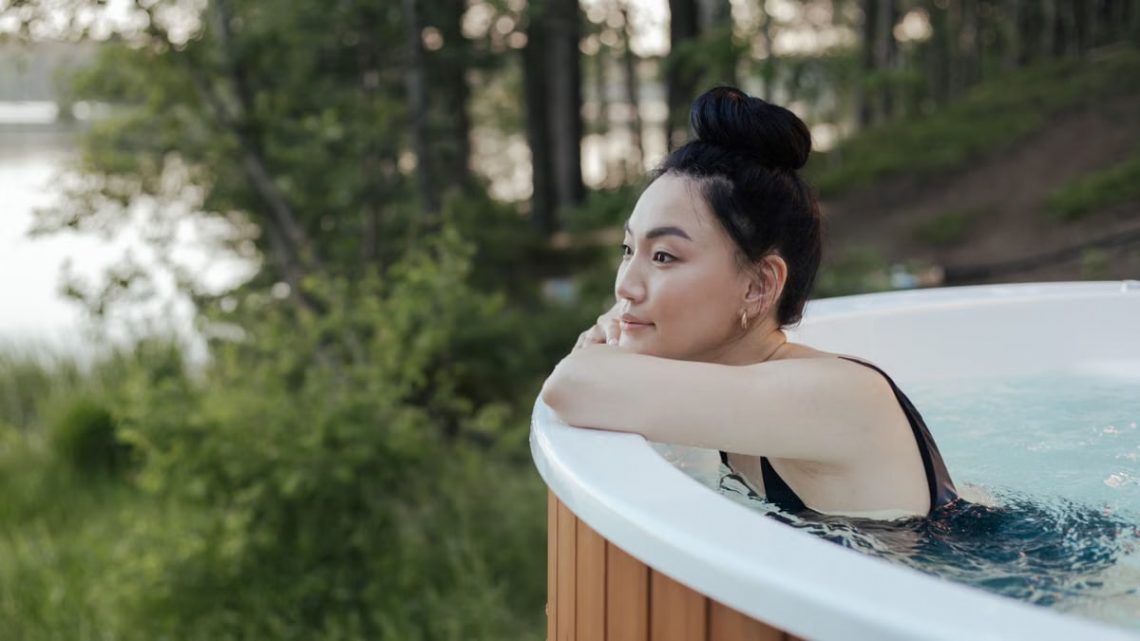 A woman in a swimsuit relaxing in an outdoor hot tub surrounded by nature, embodying leisure and wellness.