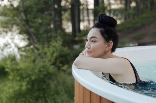 A woman in a swimsuit relaxing in an outdoor hot tub surrounded by nature, embodying leisure and wellness.